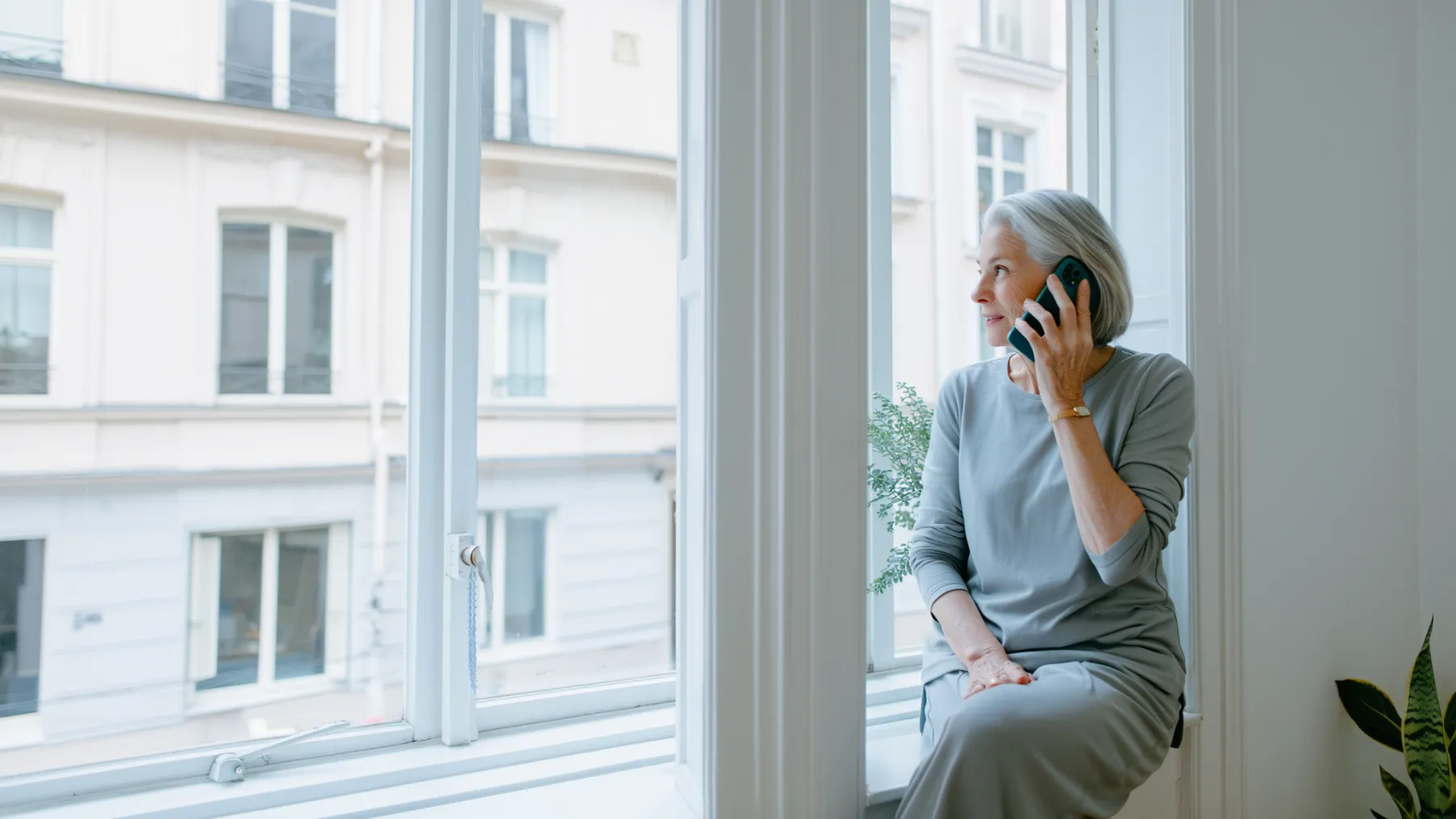 A woman in her late seventies on the phone by the window of her city apartment