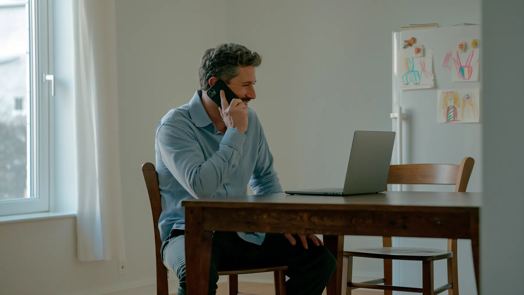 A man in his forties smiling on the phone at his family kitchen table